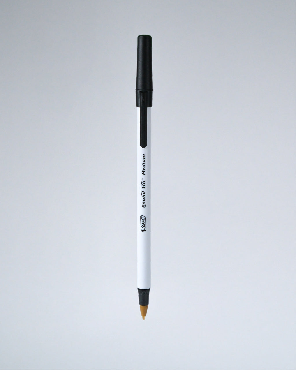 A single white and black ballpoint pen with a gold-tipped tip, shown vertically against a light gray gradient background.