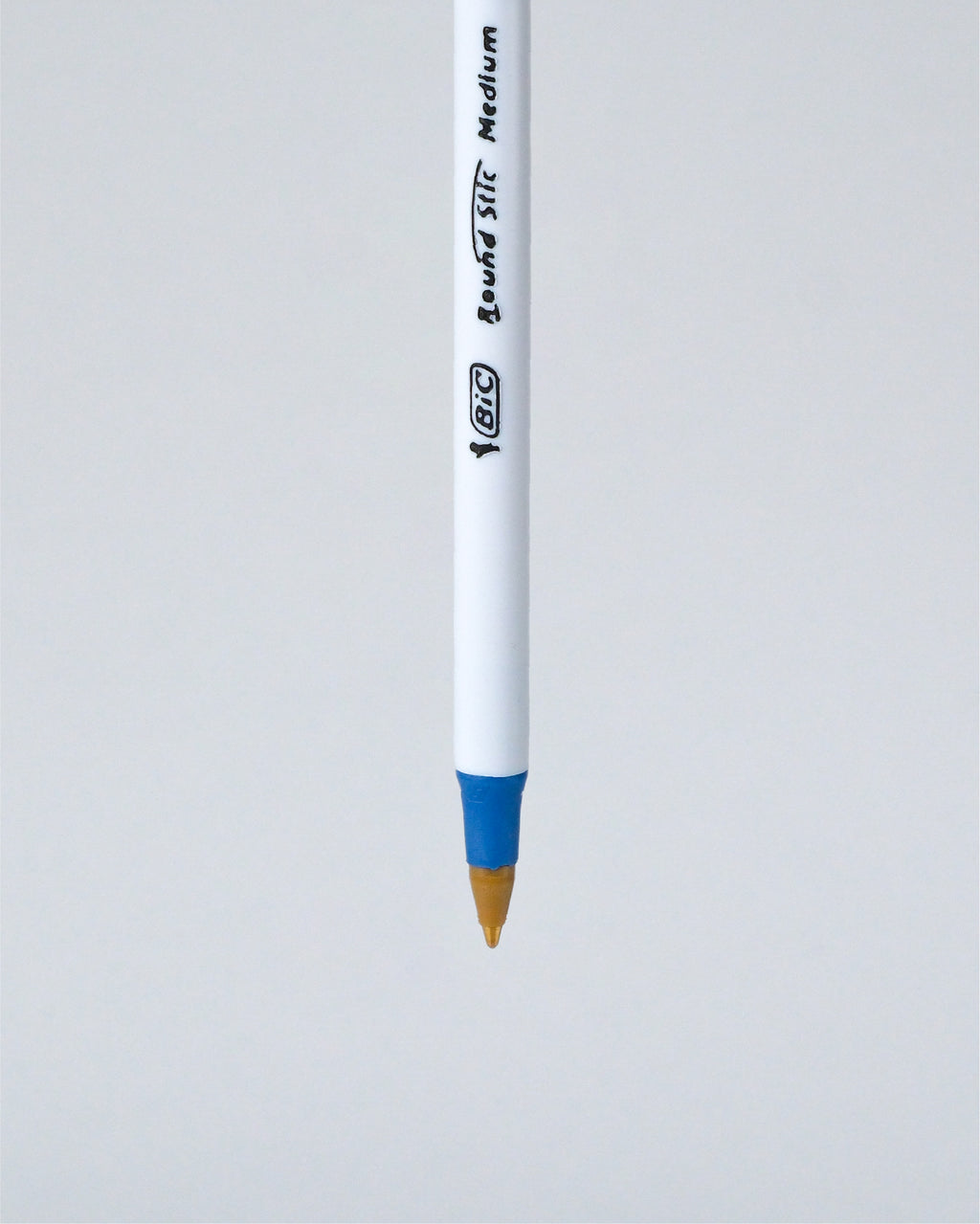 A BIC Liquid Stick Medium pen shown vertically against a light gray background, featuring a white barrel with black printed branding and a blue grip accent near the tip.