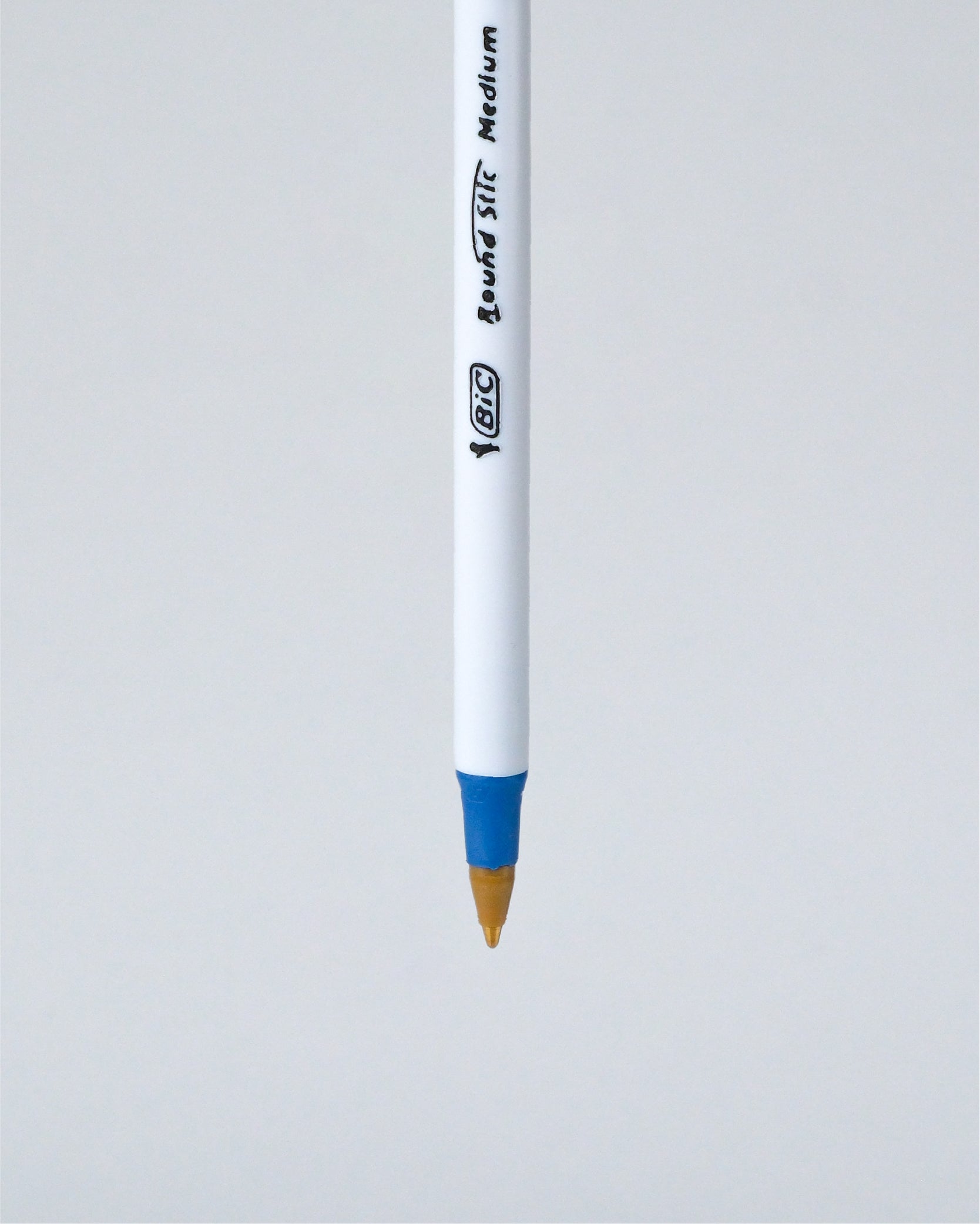 A BIC Liquid Stick Medium pen shown vertically against a light gray background, featuring a white barrel with black printed branding and a blue grip accent near the tip.