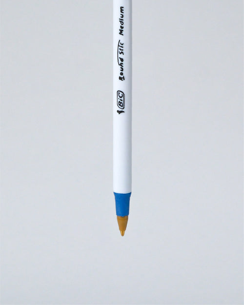 A BIC Liquid Stick Medium pen shown vertically against a light gray background, featuring a white barrel with black printed branding and a blue grip accent near the tip.