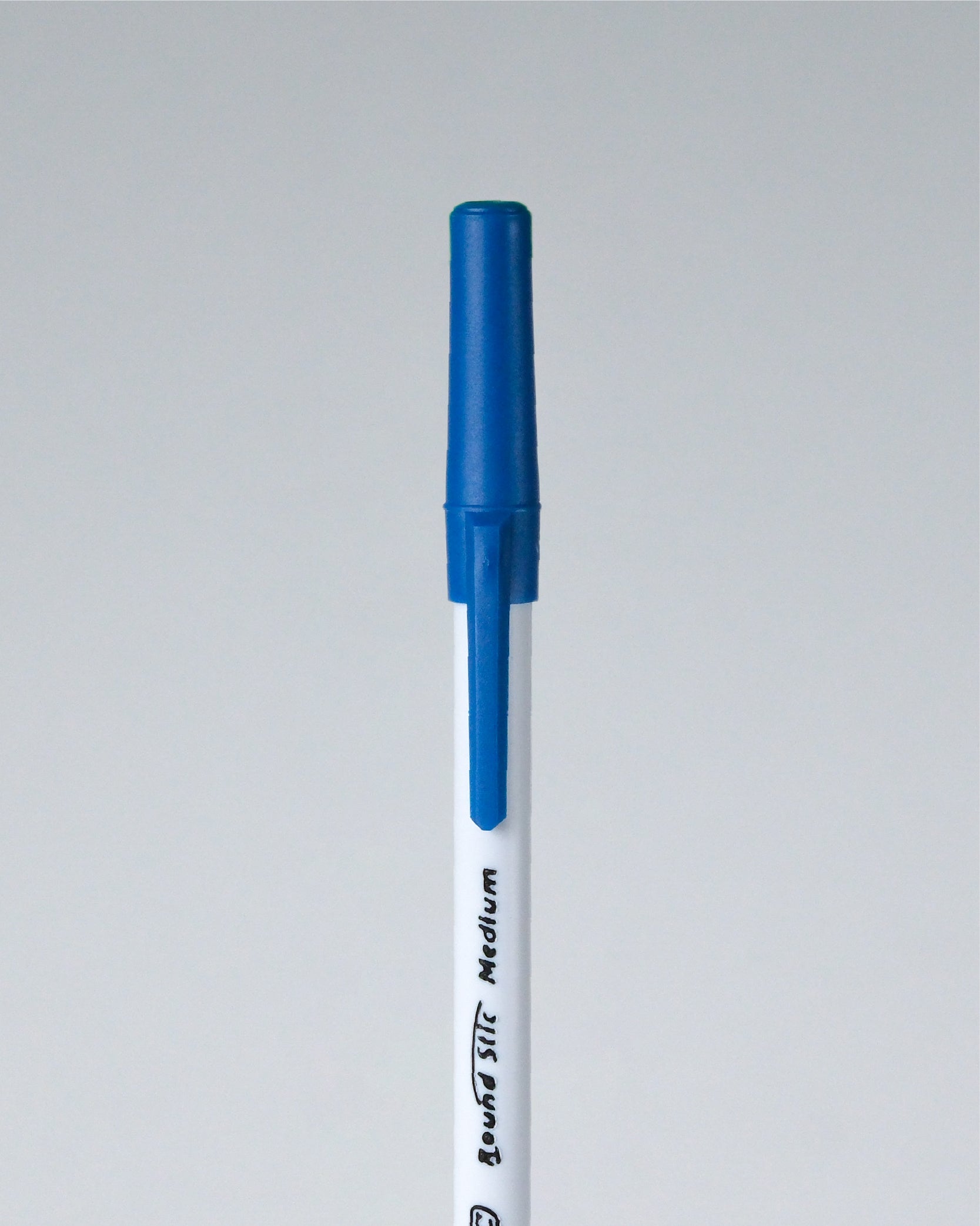 A single blue and white marker pen shown vertically against a light gray background. The barrel is white with black text reading 'Brush STI Medium', and the cap and top section are blue.