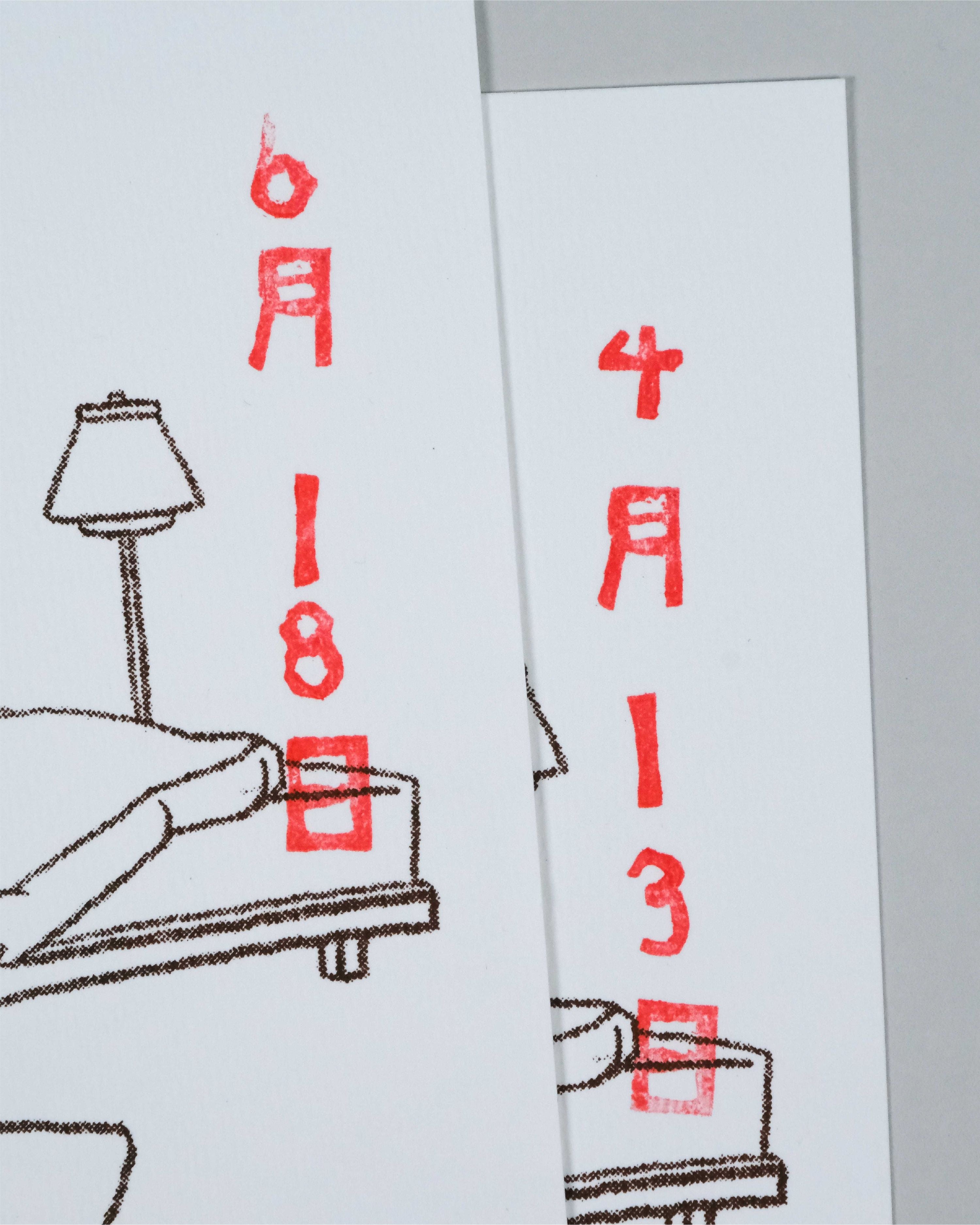 Two white rectangular cards or prints with minimalist line drawings and red stamped Japanese characters and dates, shown overlapping on a light gray background.