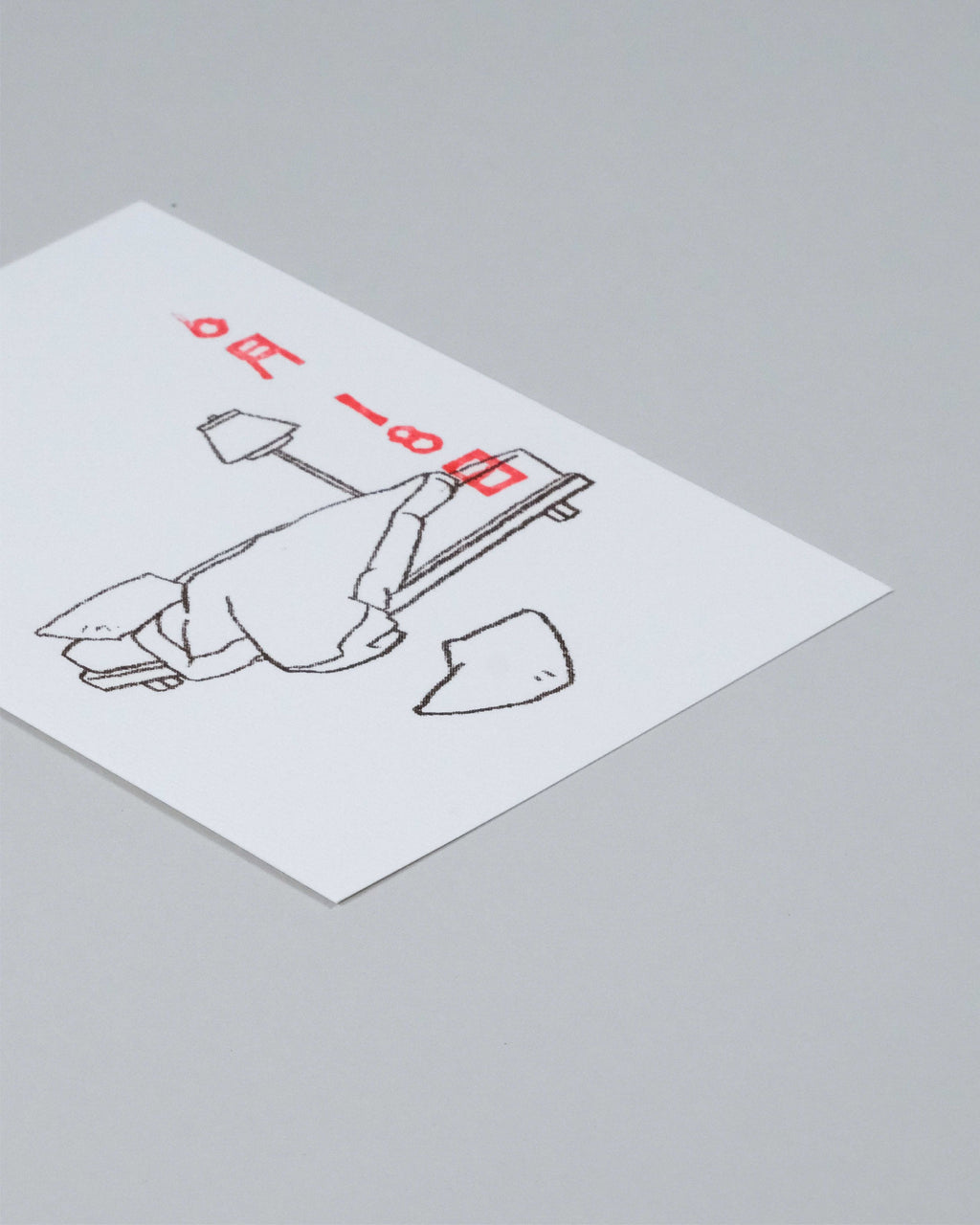 A square white art print or postcard featuring a minimalist black line drawing of a person lying on a beach chair with red text, photographed on a neutral gray background.