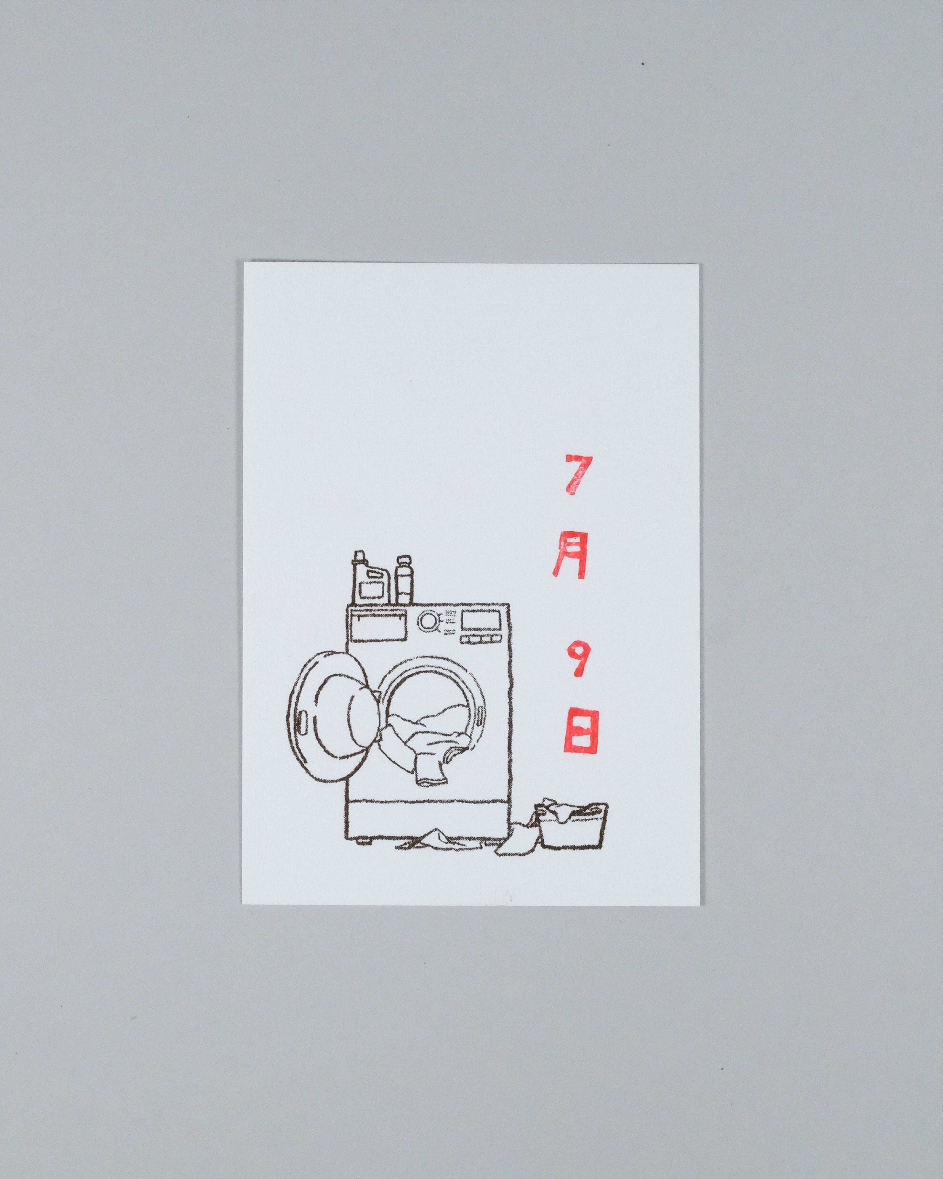 A minimalist art print featuring a black line drawing of a washing machine with red Japanese characters on a white rectangular card, set against a neutral gray background.