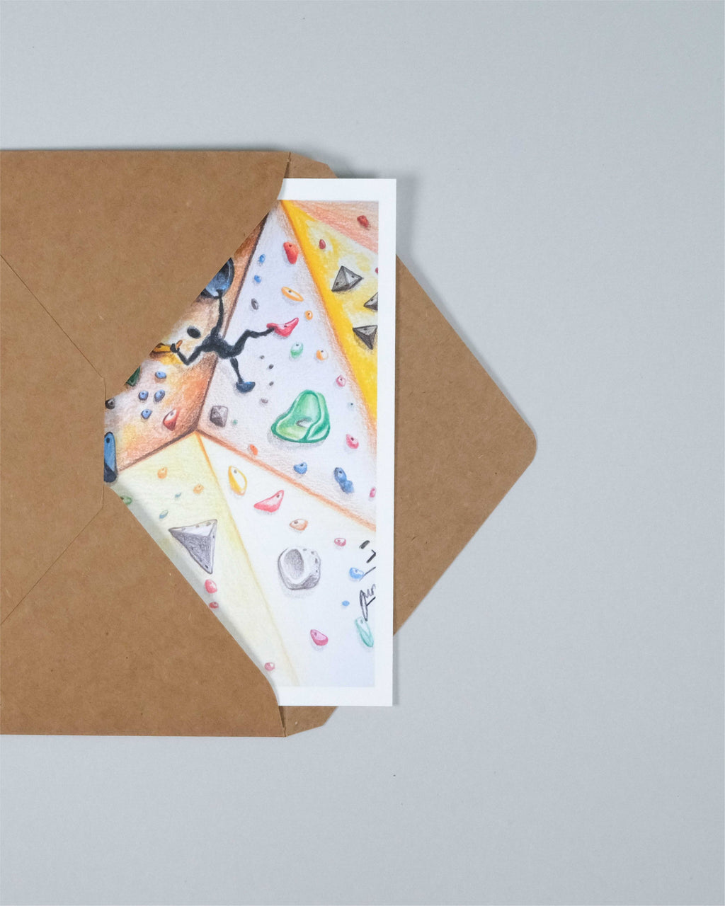 A white greeting card with a colorful climbing-themed illustration peeks out from a brown kraft paper envelope, set against a solid light gray background.