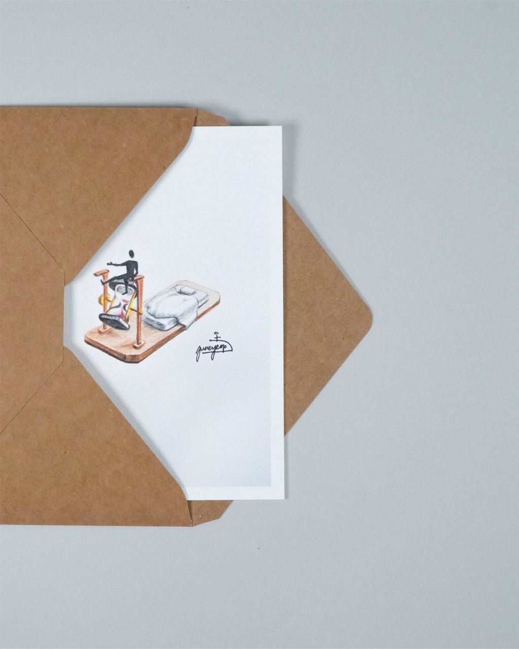 A white art print card featuring a whimsical illustration of a skeleton riding a bicycle, partially tucked inside a brown kraft paper envelope on a light gray background.