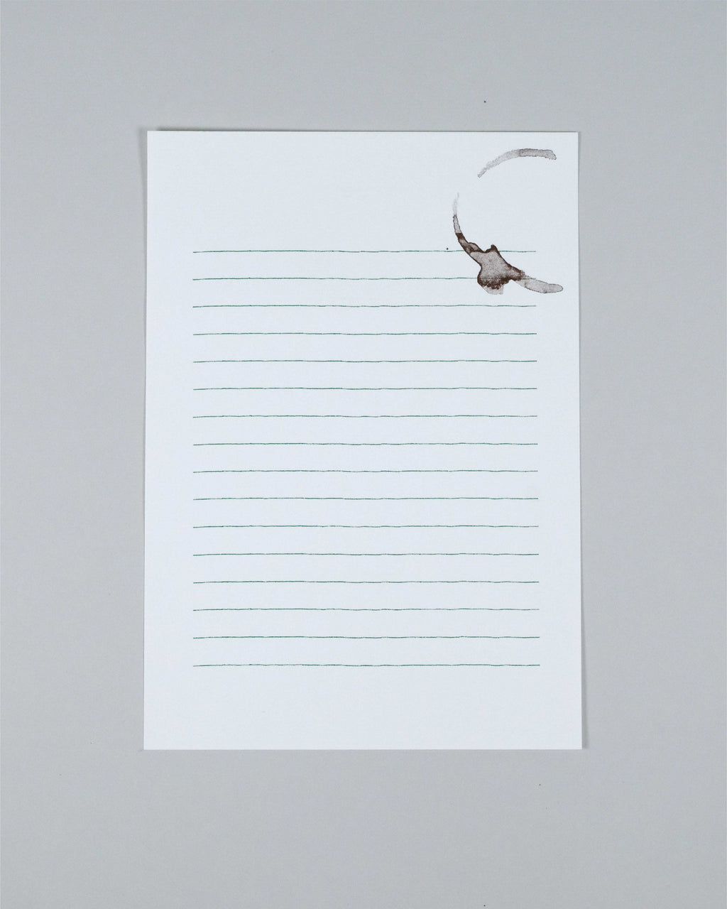A single lined notepad sheet with a white background and thin gray horizontal lines, photographed on a plain light gray surface. A faint brown coffee stain is visible near the top right corner of the pad.