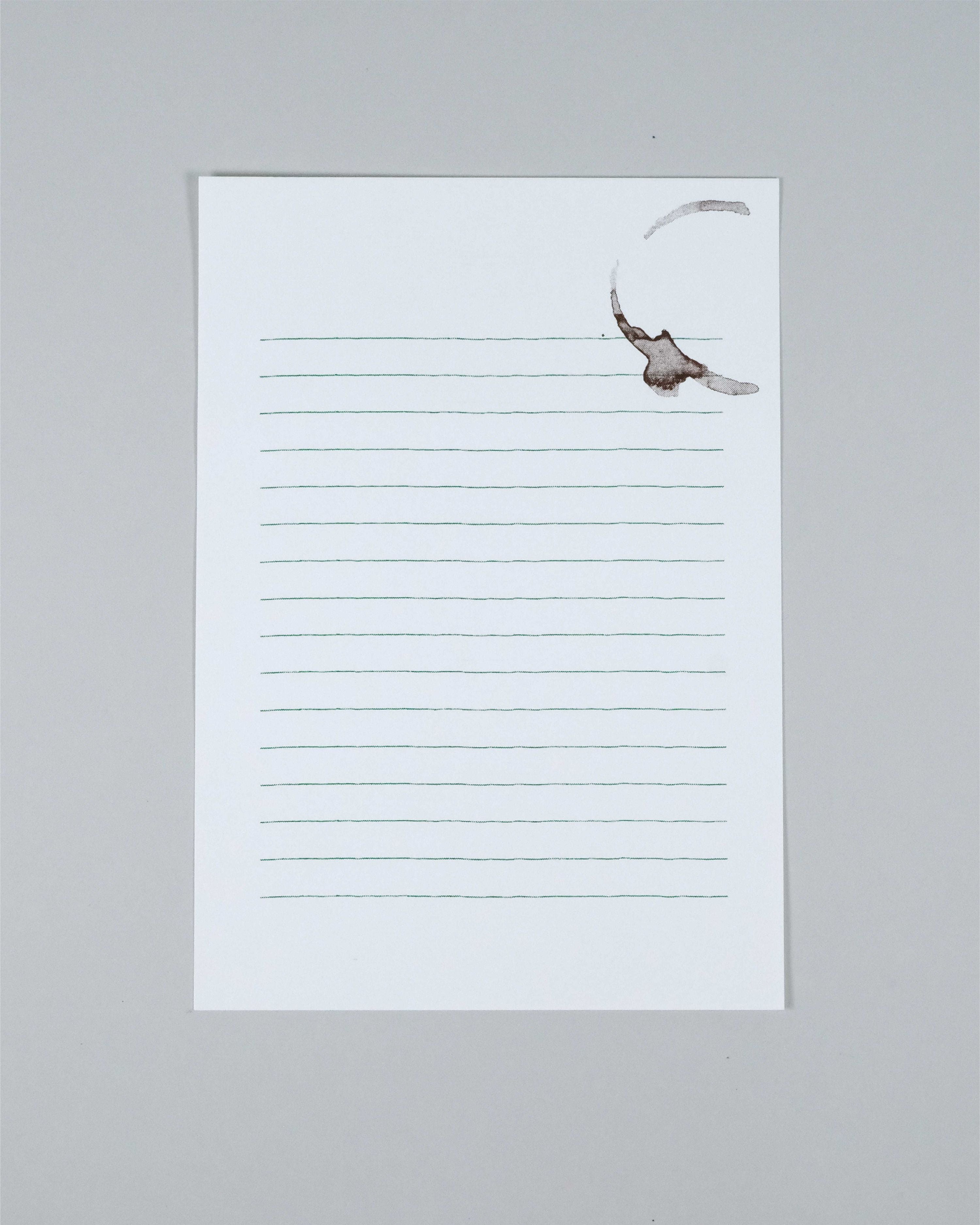 A single lined notepad sheet with a white background and thin gray horizontal lines, photographed on a plain light gray surface. A faint brown coffee stain is visible near the top right corner of the pad.