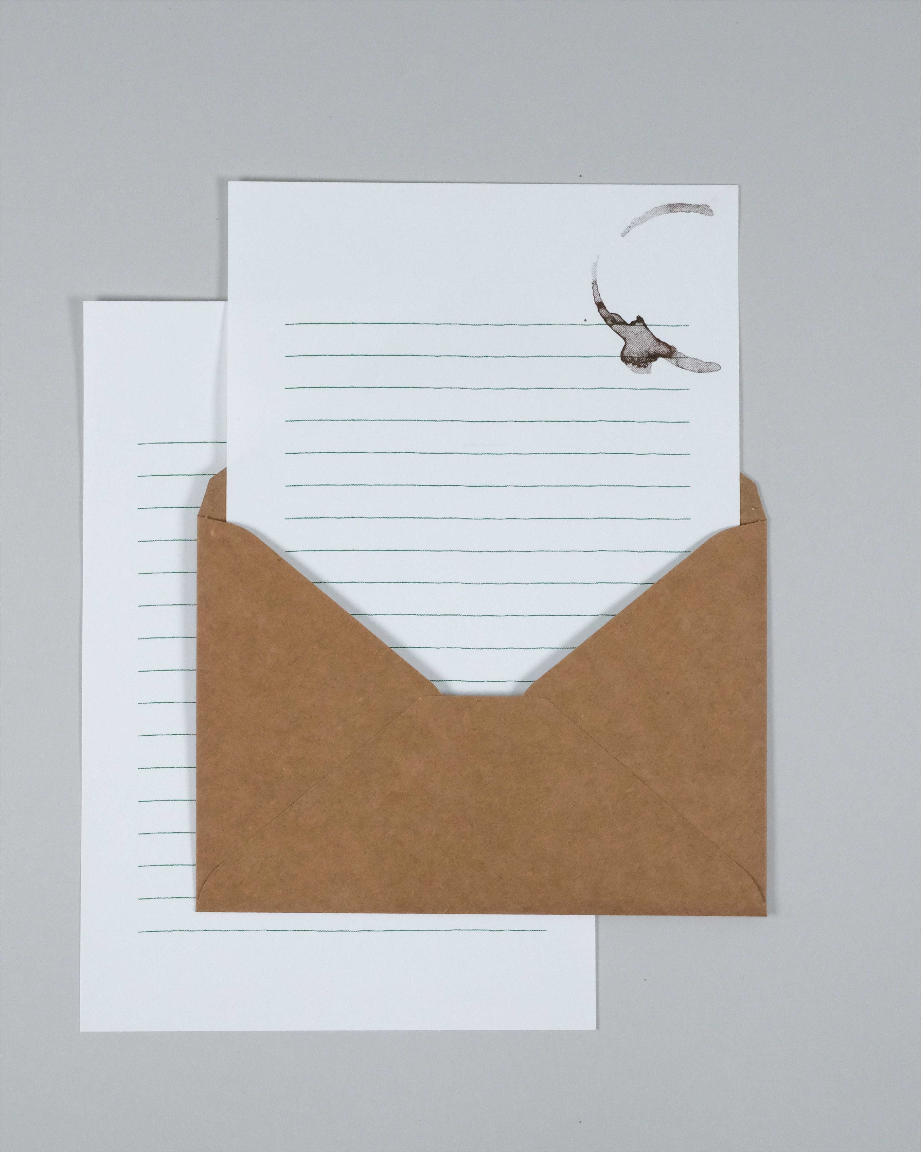 A kraft brown envelope with a white lined letterhead card partially pulled out, photographed on a plain light gray background.