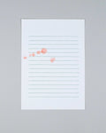 A vertical white lined notepad with faint green horizontal lines and a few scattered coral-pink watercolor dots, photographed against a light gray background.