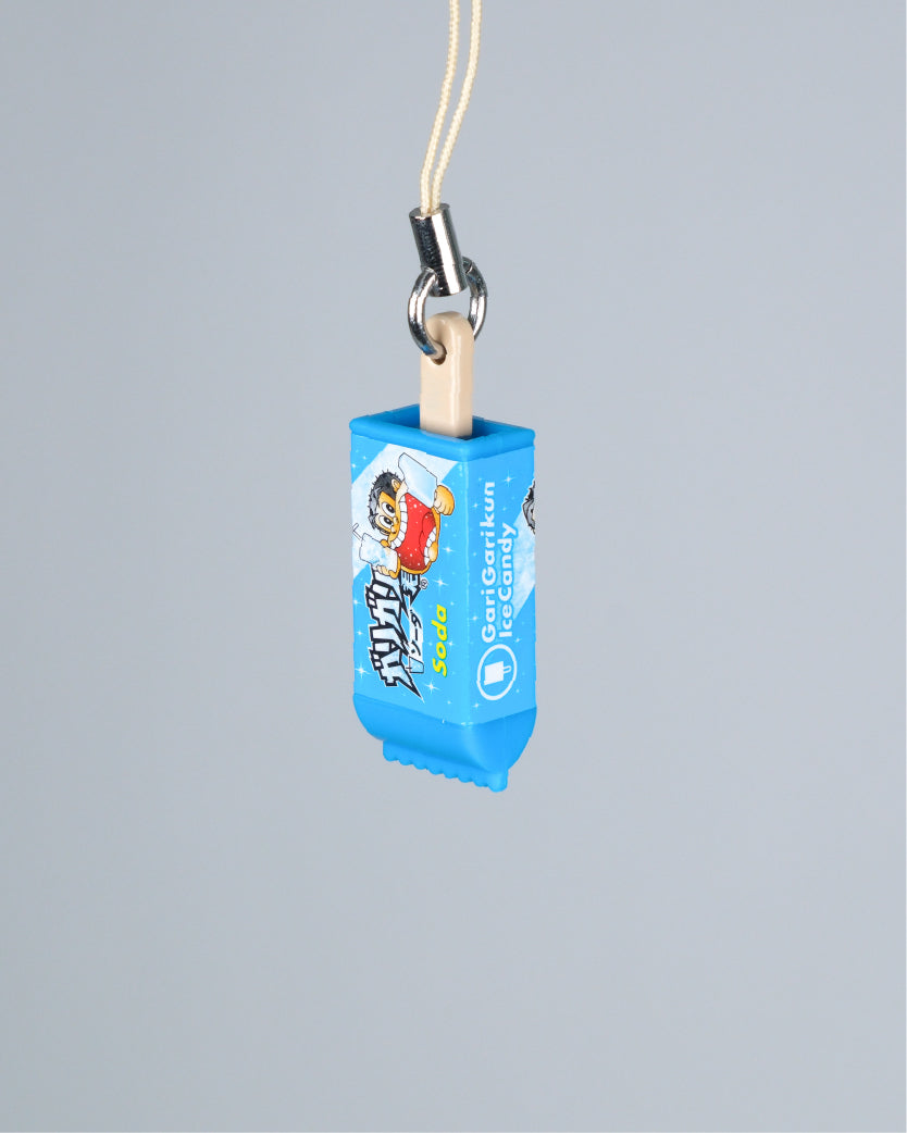 A miniature blue Sour Patch Kids toy keychain or charm with a cream-colored cord and metal clasp, shown against a solid gray background.