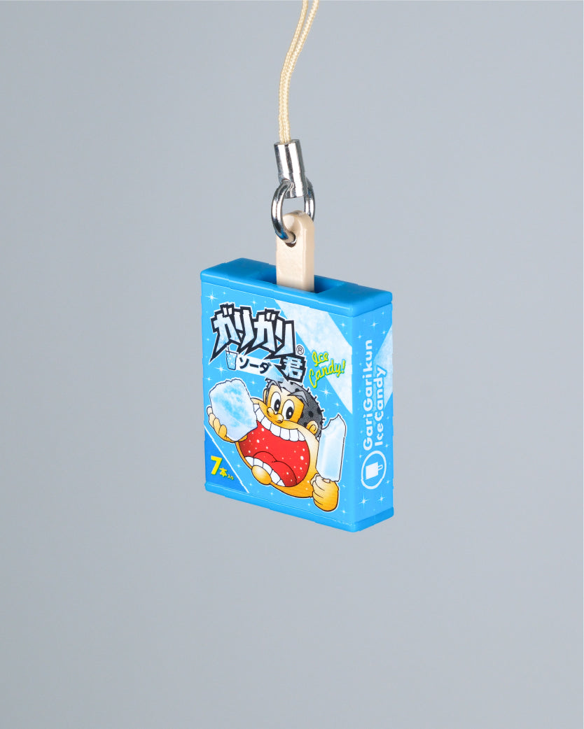 A blue rectangular novelty keychain or charm shaped like a Gari Gari ice candy box, with a cartoon character printed on the front, attached to a beige cord and silver metal clasp against a plain light gray background.