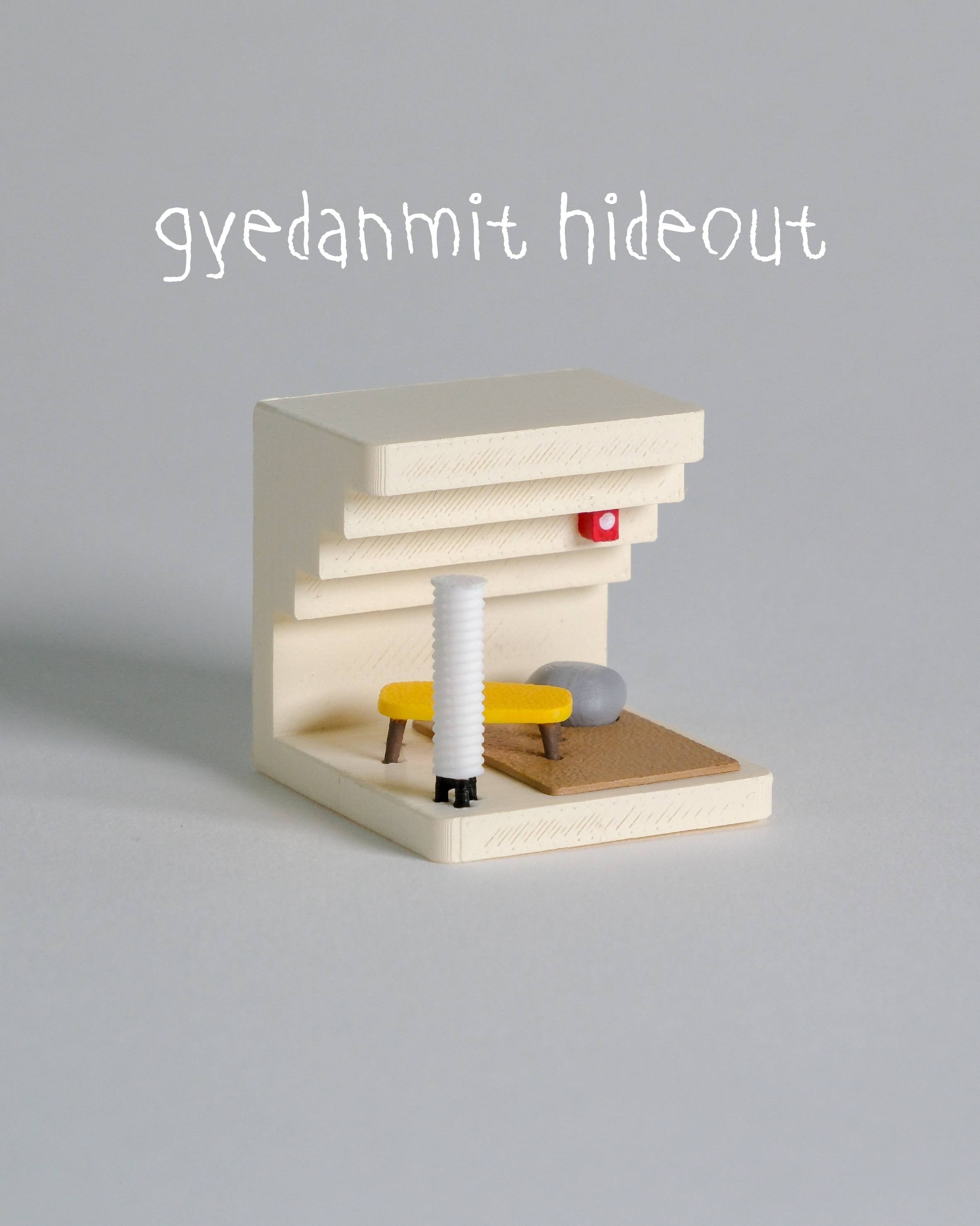 Small wooden structure with a gray top and various small items on a gray background, featuring the brand 'gyedanmit hideout'.