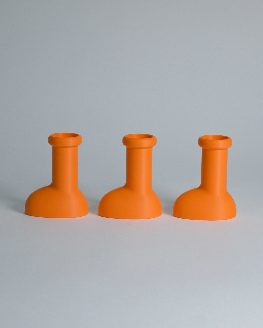 Three bright orange silicone bottle-shaped holders arranged in a row on a light gray background.