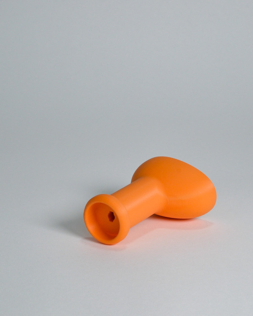 An orange silicone or rubber plug with a flared base and a short cylindrical opening, photographed on a neutral light gray background.
